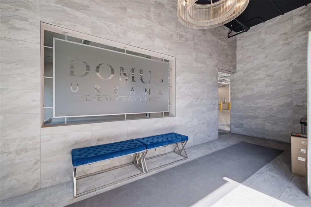 A modern lobby features a Domus Urbana sign, two blue tufted benches, and marble-patterned walls — 644 3RD AVENUE S UNIT 403, ST PETERSBURG, FL
