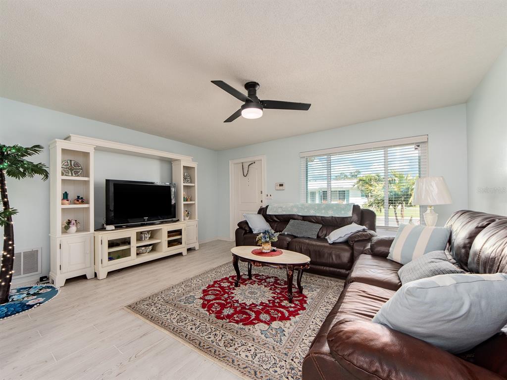 A living room features light wood-look flooring, a white entertainment center, and brown leather sofas — 14104 88TH AVENUE, SEMINOLE, FL