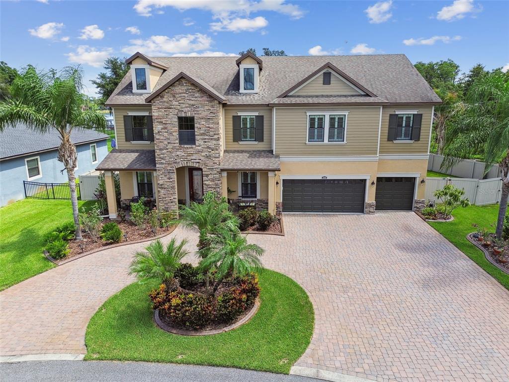 A two-story suburban house with a stone facade, beige siding, and a paved circular driveway — 2566 LAKE MANOR DRIVE, LAND O LAKES, FL