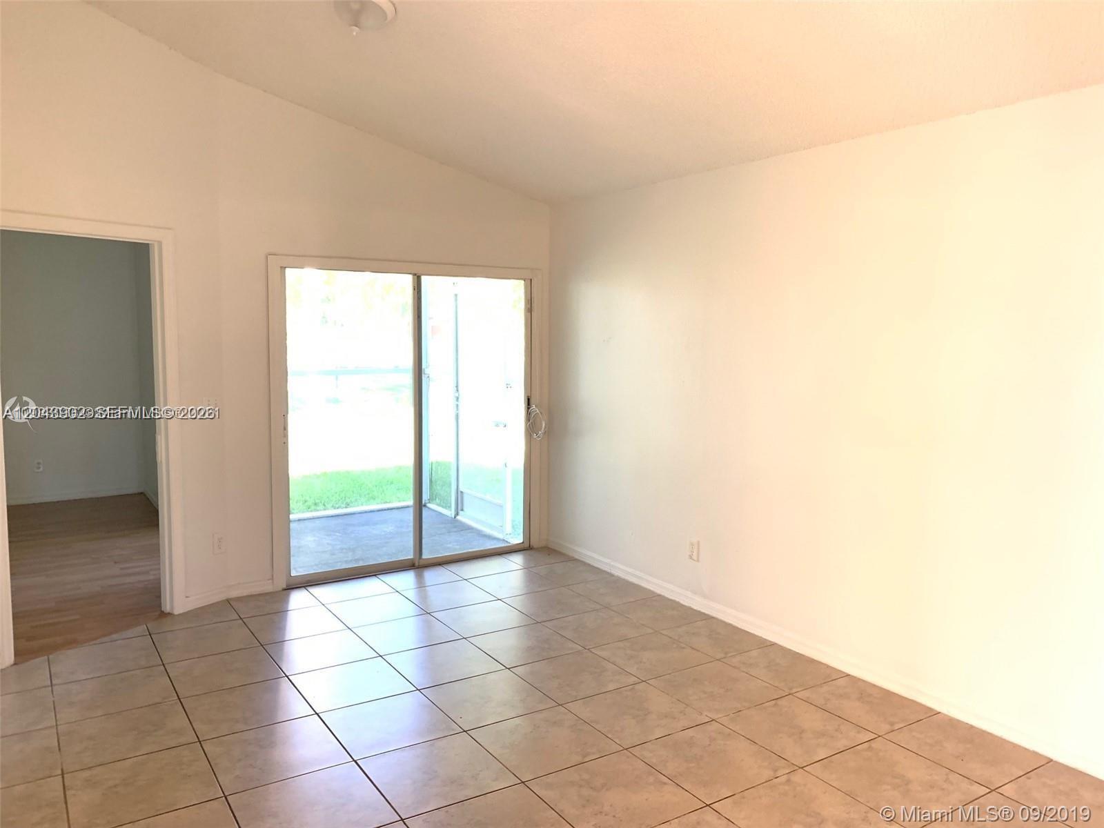 This room features light-colored tile flooring, white walls, and a sliding glass door to a patio — 848 SW 10th St, Florida City FL 33034, FLORIDA CITY, FL