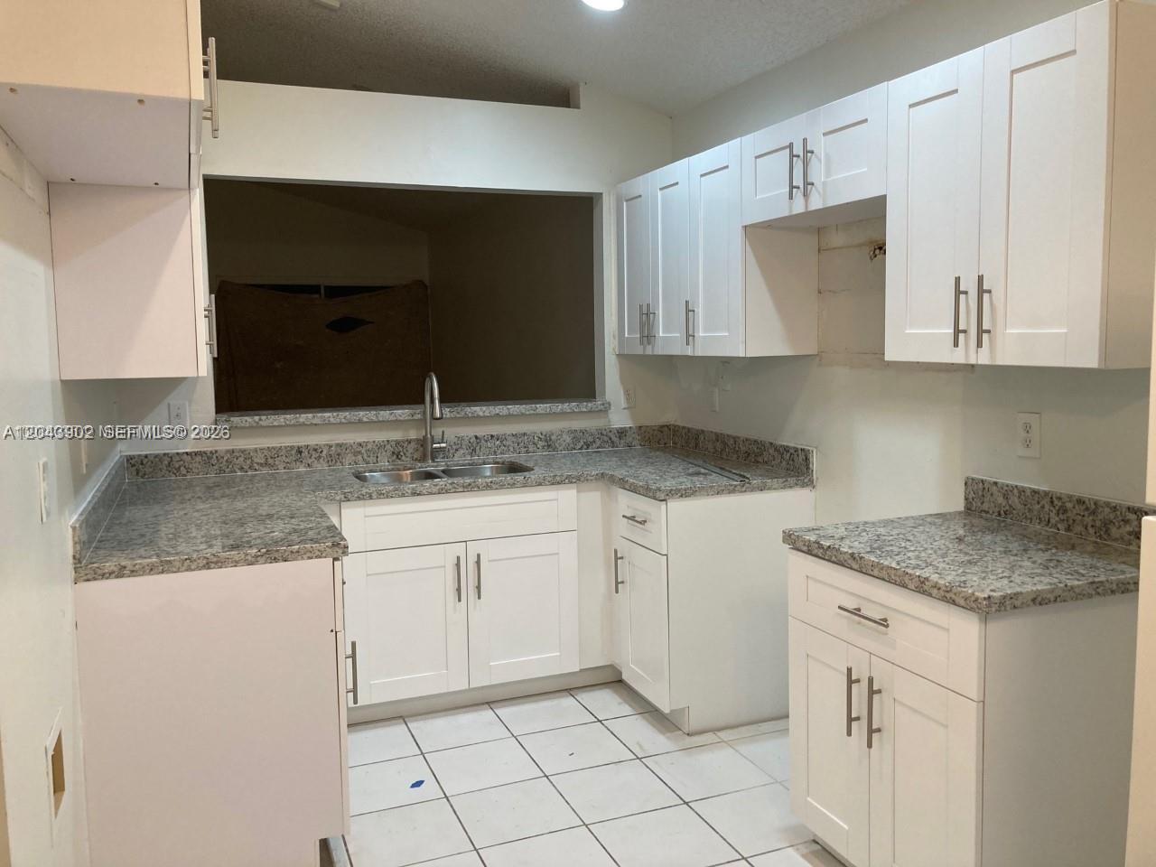 A kitchen features white cabinets, granite countertops, and a pass-through window above the sink — 848 SW 10th St, Florida City FL 33034, FLORIDA CITY, FL