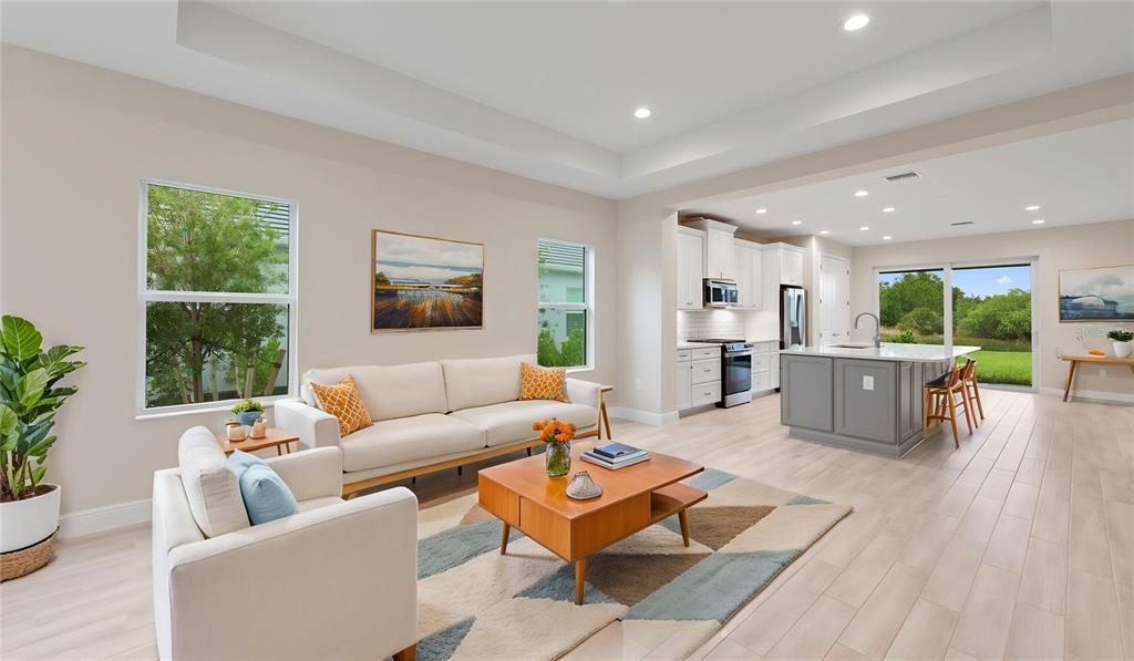 An open-concept living room and kitchen featuring light wood floors, white cabinetry, and large windows — 2937 HERITAGE PINES DRIVE, FORT MYERS, FL
