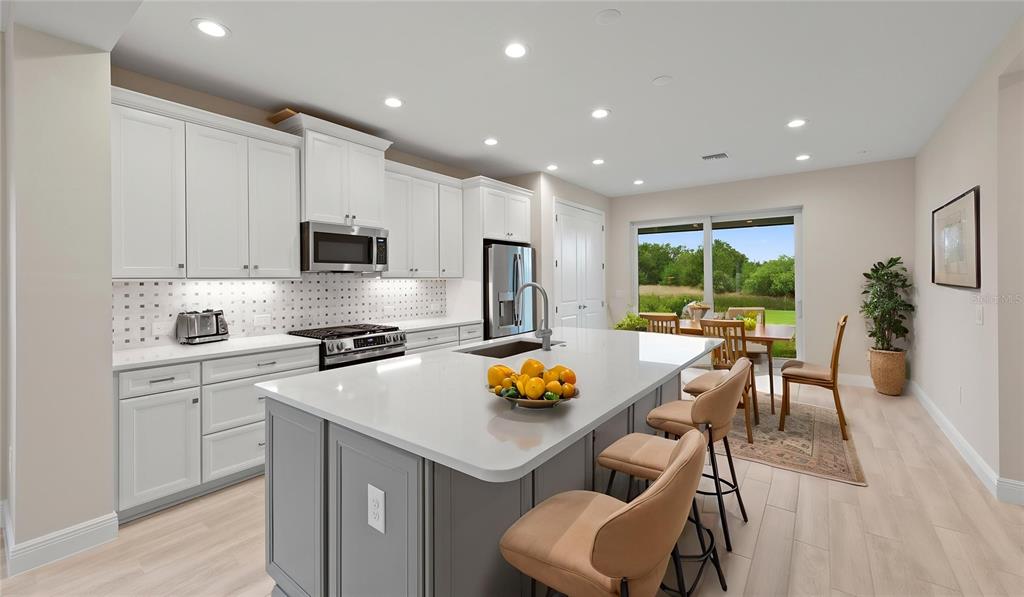 A modern kitchen features white cabinets, a gray island with bar stools, and dining area — 2937 HERITAGE PINES DRIVE, FORT MYERS, FL