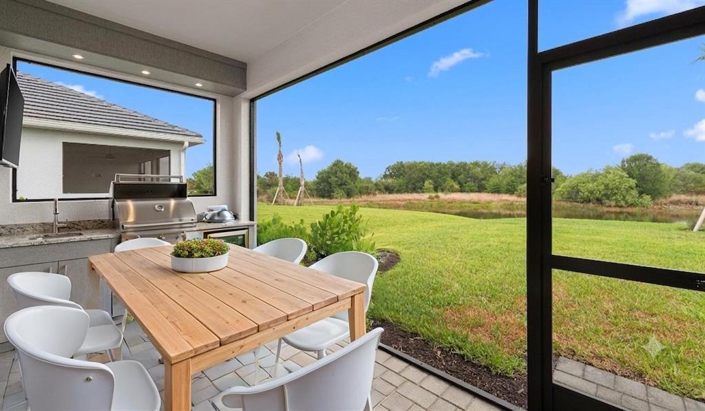 A screened-in patio features a wooden dining table, outdoor kitchen, and views of a grassy yard — 2937 HERITAGE PINES DRIVE, FORT MYERS, FL