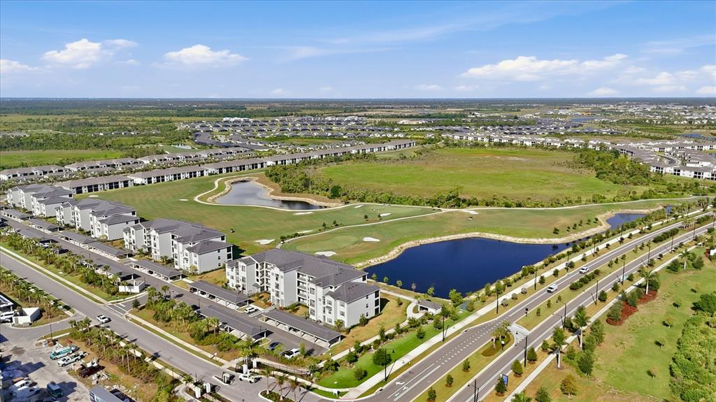 An aerial view shows apartment buildings, a golf course, and a pond near a road — 17655 OPAL SAND DRIVE UNIT 107, VENICE, FL