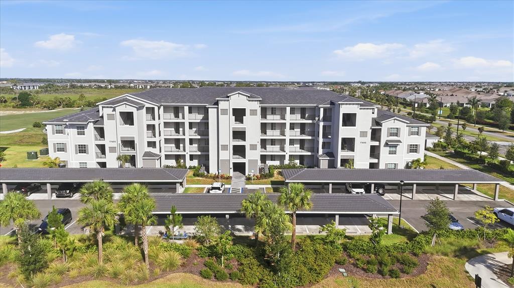 An exterior view of a multi-story apartment building with covered parking structures in the foreground — 17655 OPAL SAND DRIVE UNIT 107, VENICE, FL
