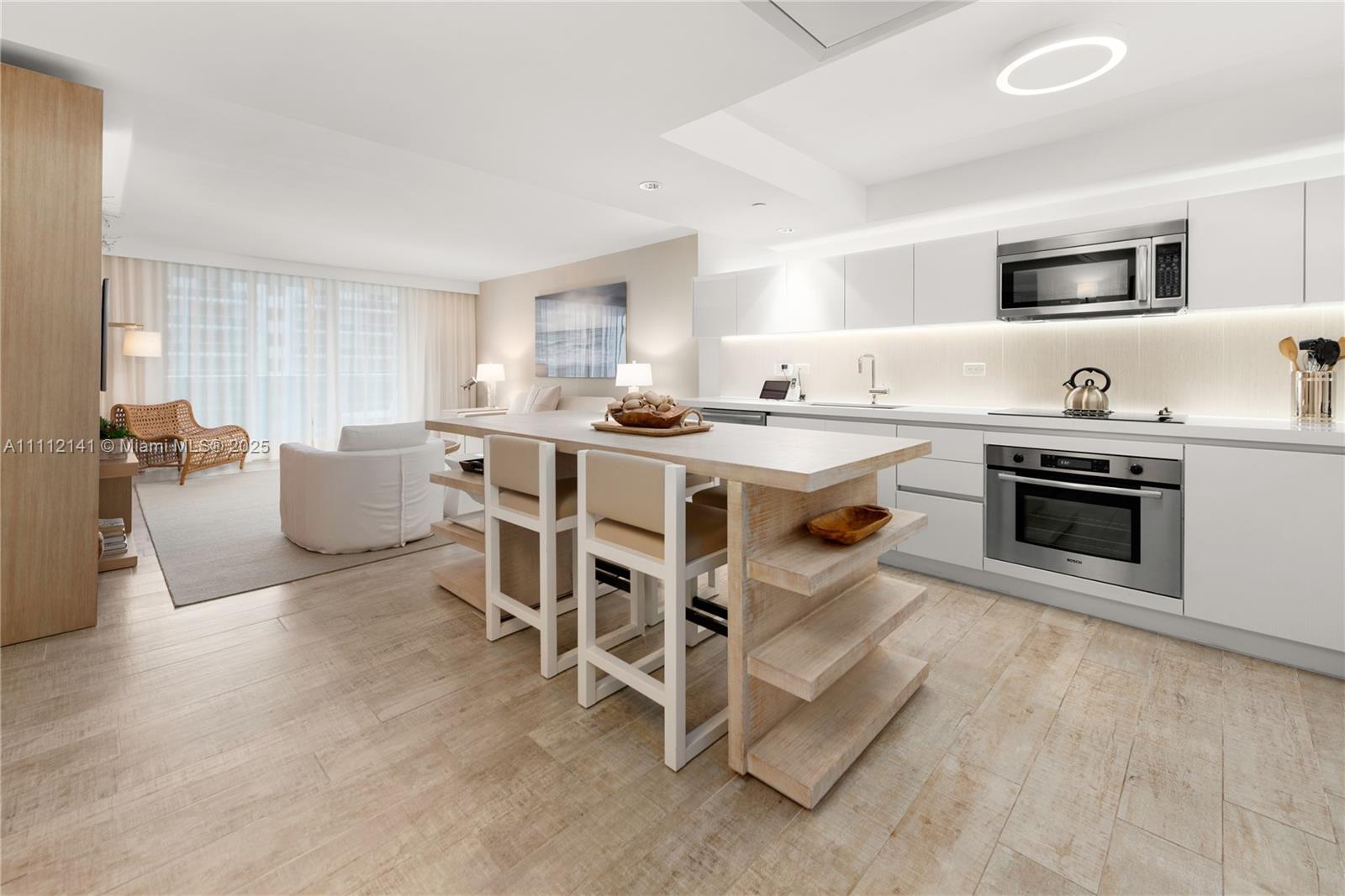 A modern kitchen with white cabinetry and a wooden island sits in an open-plan room — 102 24th St # 1208, Miami Beach FL 33139, MIAMI BEACH, FL