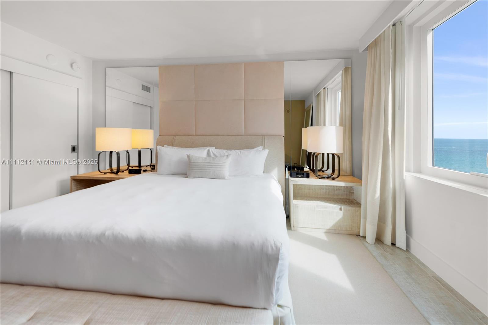 A bedroom features a bed with a tufted headboard, mirrored walls, and an ocean view — 102 24th St # 1208, Miami Beach FL 33139, MIAMI BEACH, FL