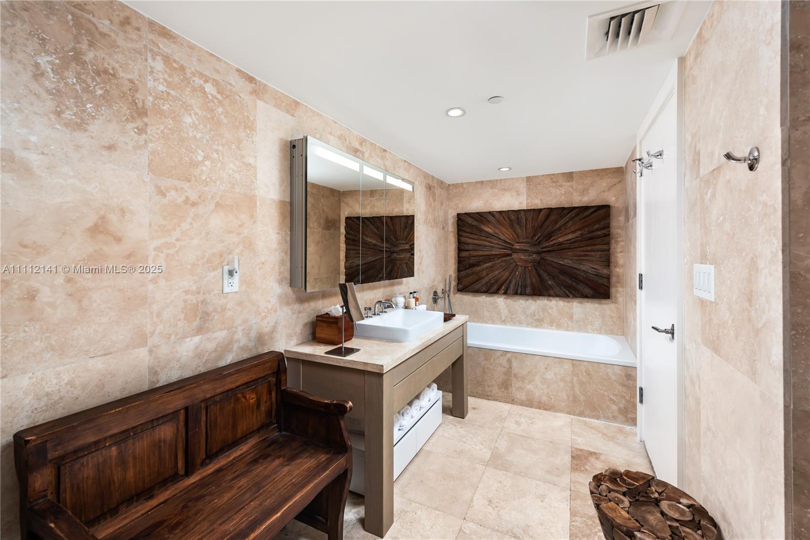 A bathroom features travertine tile walls and floors, a wooden bench, and a soaking tub — 102 24th St # 1208, Miami Beach FL 33139, MIAMI BEACH, FL
