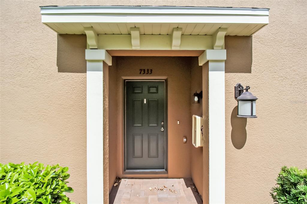 The front entrance of a house features a dark door, a white portico, and a lantern — 7333 SKYBIRD ROAD, BRADENTON, FL