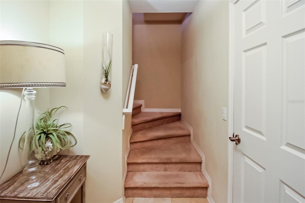 A carpeted staircase leads upward between a side table with a lamp and a white door — 7333 SKYBIRD ROAD, BRADENTON, FL