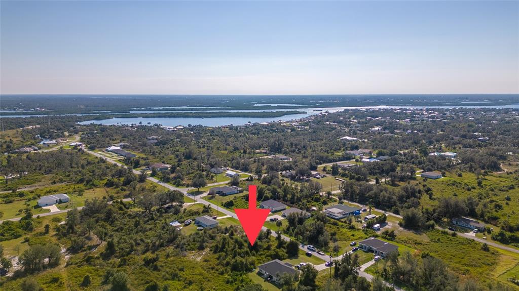 An aerial view shows a vacant, wooded lot marked by a red arrow near houses — 27100 27096 PARTIN DRIVE UNIT 0, PUNTA GORDA, FL