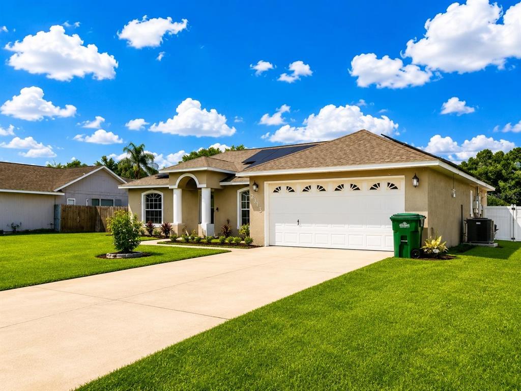 A single-story house with a tan stucco exterior, a two-car garage, and a green trash bin — 2333 AINSWORTH AVENUE, DELTONA, FL
