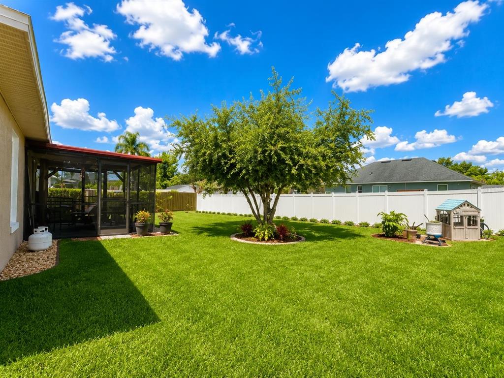 A backyard features a green lawn, a large central tree, and a screened-in patio — 2333 AINSWORTH AVENUE, DELTONA, FL