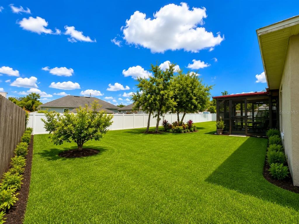 A grassy backyard features a small tree, a screened-in porch, and a white vinyl fence — 2333 AINSWORTH AVENUE, DELTONA, FL