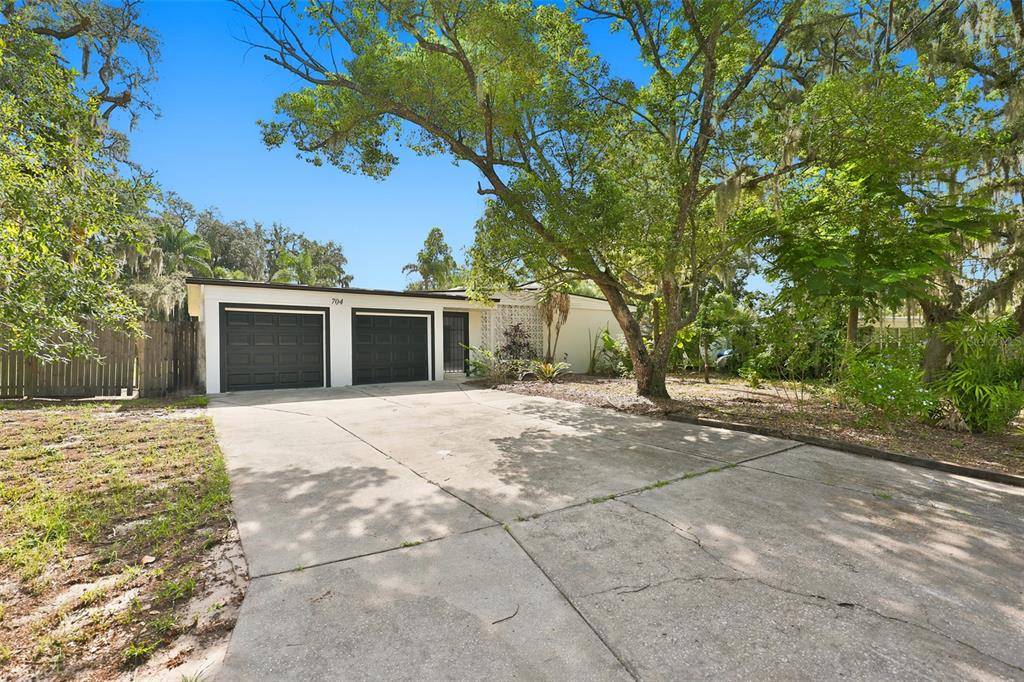 A single-story house with a two-car garage and a concrete driveway under large trees — 704 E RIVER DRIVE, TAMPA, FL