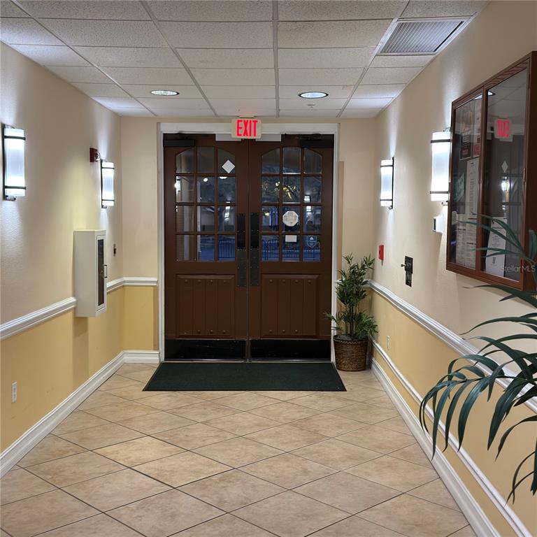 A tiled hallway leads to a set of double brown doors with an exit sign — 13941 CLUBHOUSE DRIVE UNIT 208, TAMPA, FL