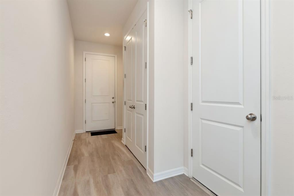 A hallway with light wood-look flooring leads to a white door with three interior doors — 1524 BLUE SEA STREET, CLEARWATER, FL