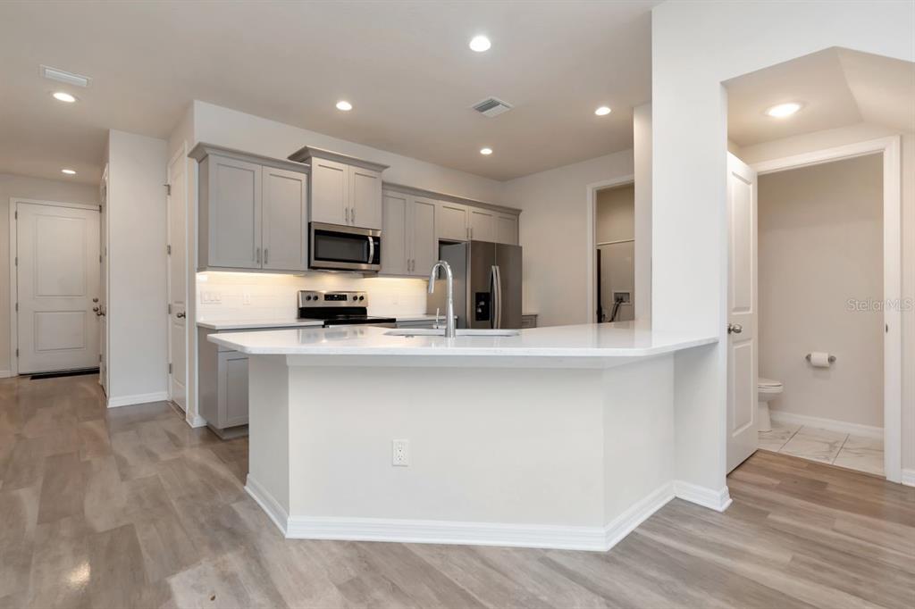 A modern kitchen features gray cabinets, stainless steel appliances, and a white quartz breakfast bar — 1524 BLUE SEA STREET, CLEARWATER, FL
