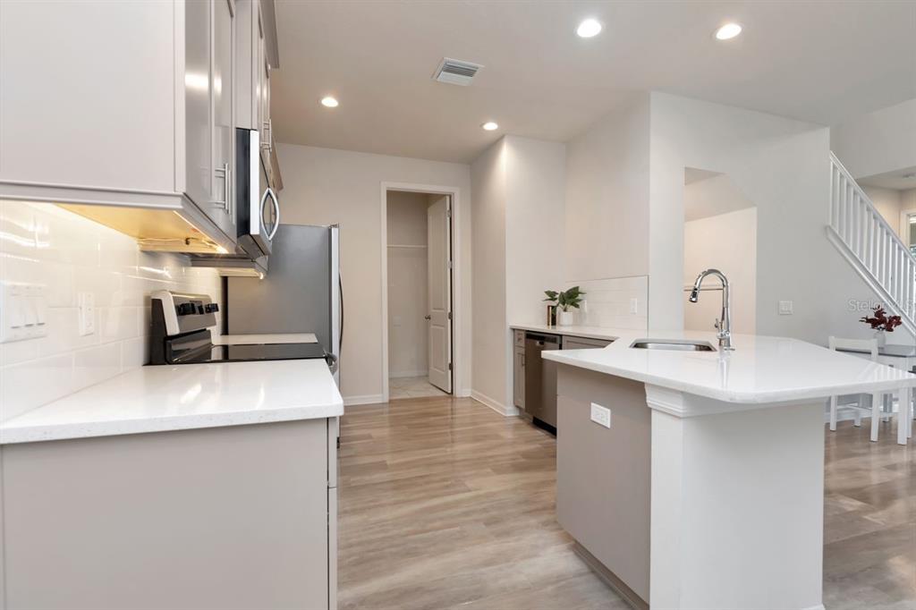 A modern kitchen features light-colored cabinetry, white countertops, stainless steel appliances, and wood-look flooring — 1524 BLUE SEA STREET, CLEARWATER, FL
