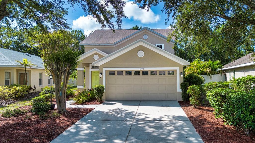 A two-story suburban house features a tan stucco exterior, a two-car garage, and landscaping — 14246 TREE SWALLOW WAY, LAKEWOOD RANCH, FL