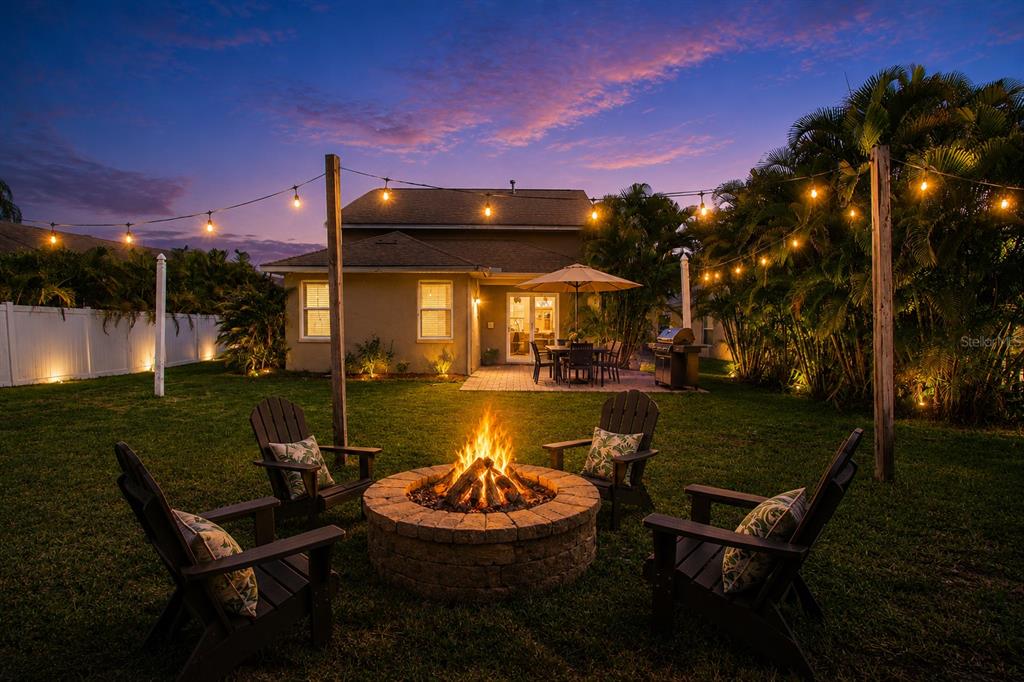 A backyard features a stone fire pit with Adirondack chairs under string lights at dusk — 14246 TREE SWALLOW WAY, LAKEWOOD RANCH, FL