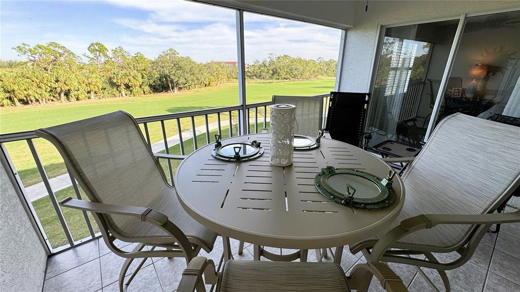 A screened-in balcony features a round dining table with chairs overlooking a grassy field — 8735 OLDE HICKORY AVENUE UNIT 8306, SARASOTA, FL