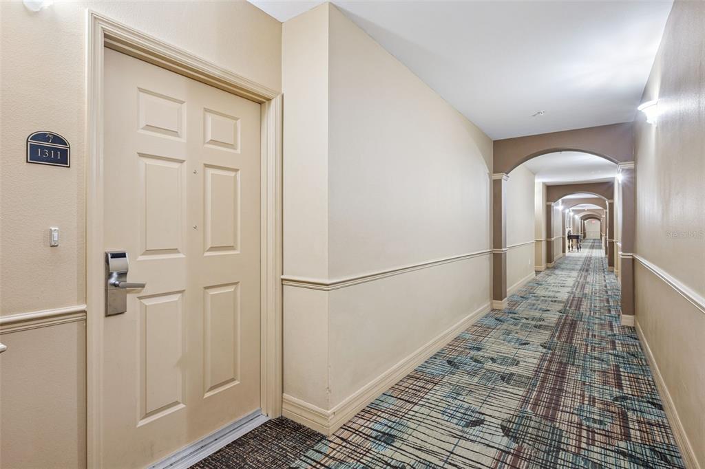 A hallway with patterned carpet leads past a door labeled 1311 toward distant arches — 8112 POINCIANA BOULEVARD UNIT 1311, ORLANDO, FL