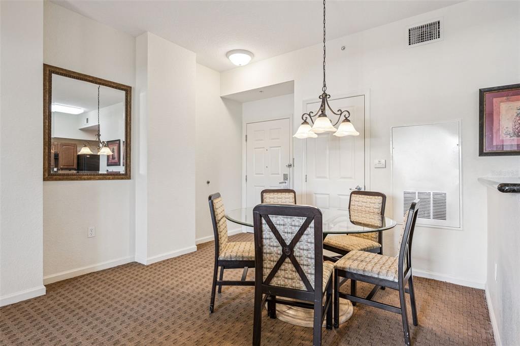 A dining area features a glass-topped table with four chairs, a chandelier, and carpeted flooring — 8112 POINCIANA BOULEVARD UNIT 1311, ORLANDO, FL