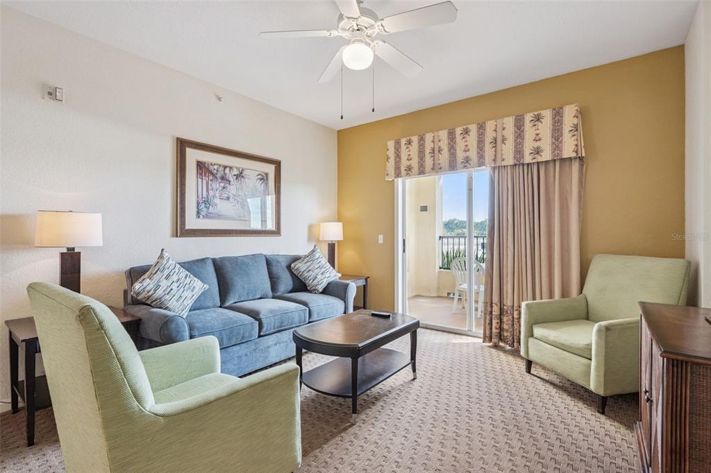A living room features a blue sofa, two light green armchairs, and a sliding glass door — 8112 POINCIANA BOULEVARD UNIT 1311, ORLANDO, FL