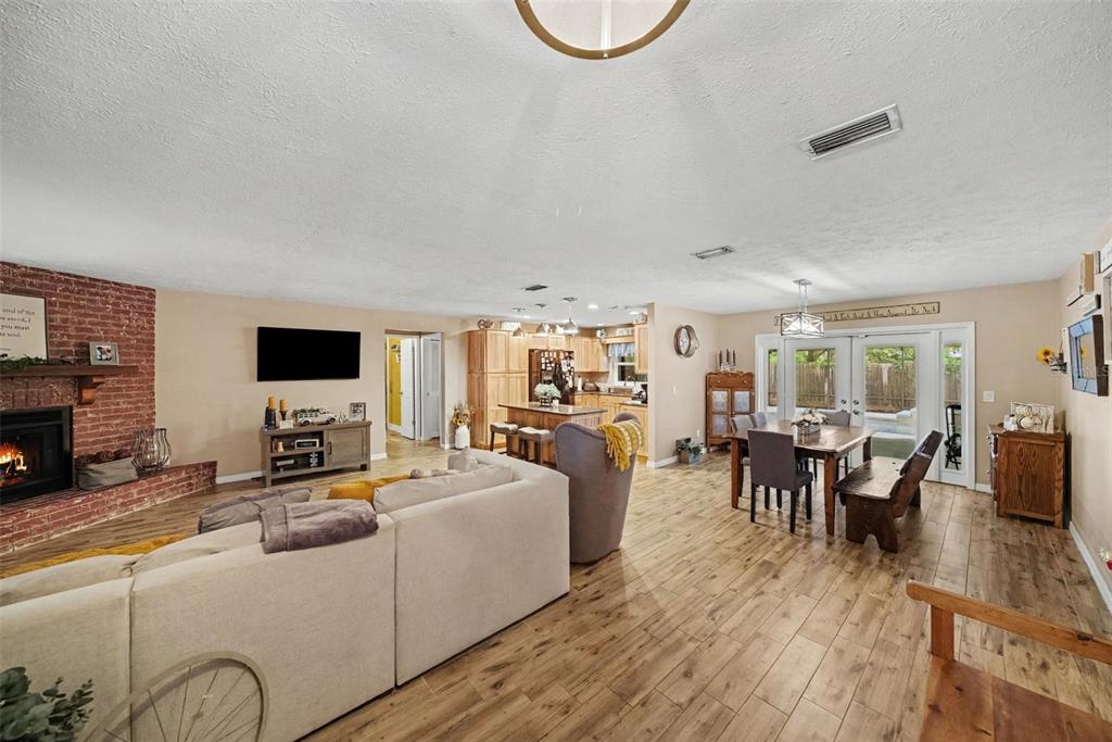 An open-concept living and dining area features wood-look flooring, a brick fireplace, and kitchen access — 206 JACOB RYAN COURT, BRANDON, FL