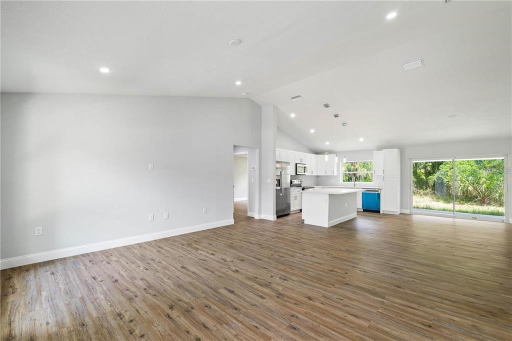 An open-concept living area with wood-look flooring, vaulted ceilings, and a modern white kitchen — 19191 WILLARD AVENUE, PORT CHARLOTTE, FL