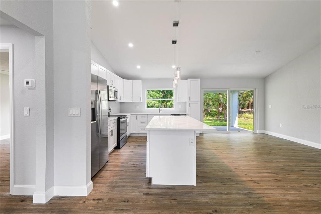 A modern kitchen features white cabinets, a central island, and wood-look flooring — 19191 WILLARD AVENUE, PORT CHARLOTTE, FL