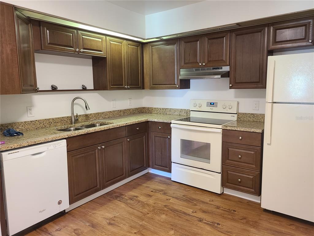 A kitchen features dark wood cabinets, granite countertops, white appliances, and wood-look flooring — 5427 PEACO PLACE, WINTER PARK, FL