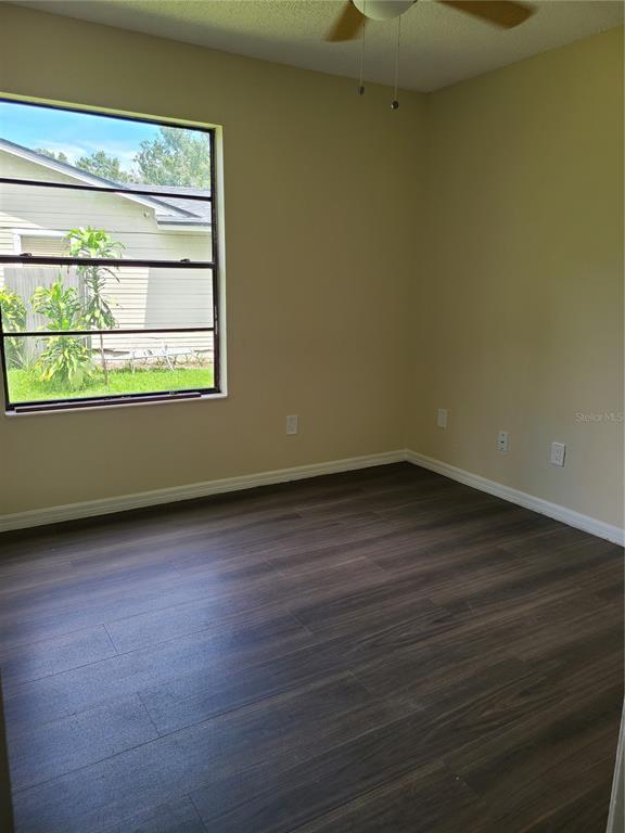 An empty bedroom features dark wood-look flooring, beige walls, and a window overlooking a yard — 5427 PEACO PLACE, WINTER PARK, FL