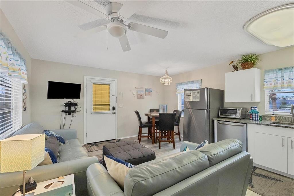 A living room and kitchen area with a dining table, ceiling fan, and gray sofas — 301 AVENIDA MADERA UNIT A, SARASOTA, FL