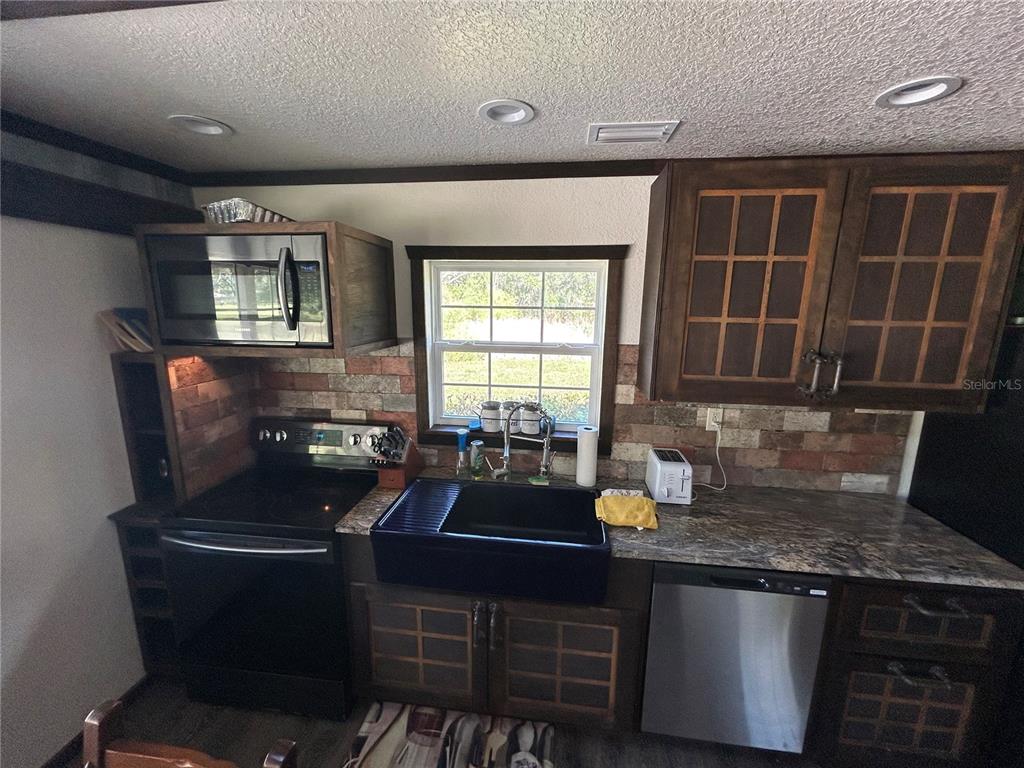 A kitchen features dark wood cabinets, a black farmhouse sink, and a brick-style backsplash — 15455 NW 100TH AVENUE ROAD, REDDICK, FL