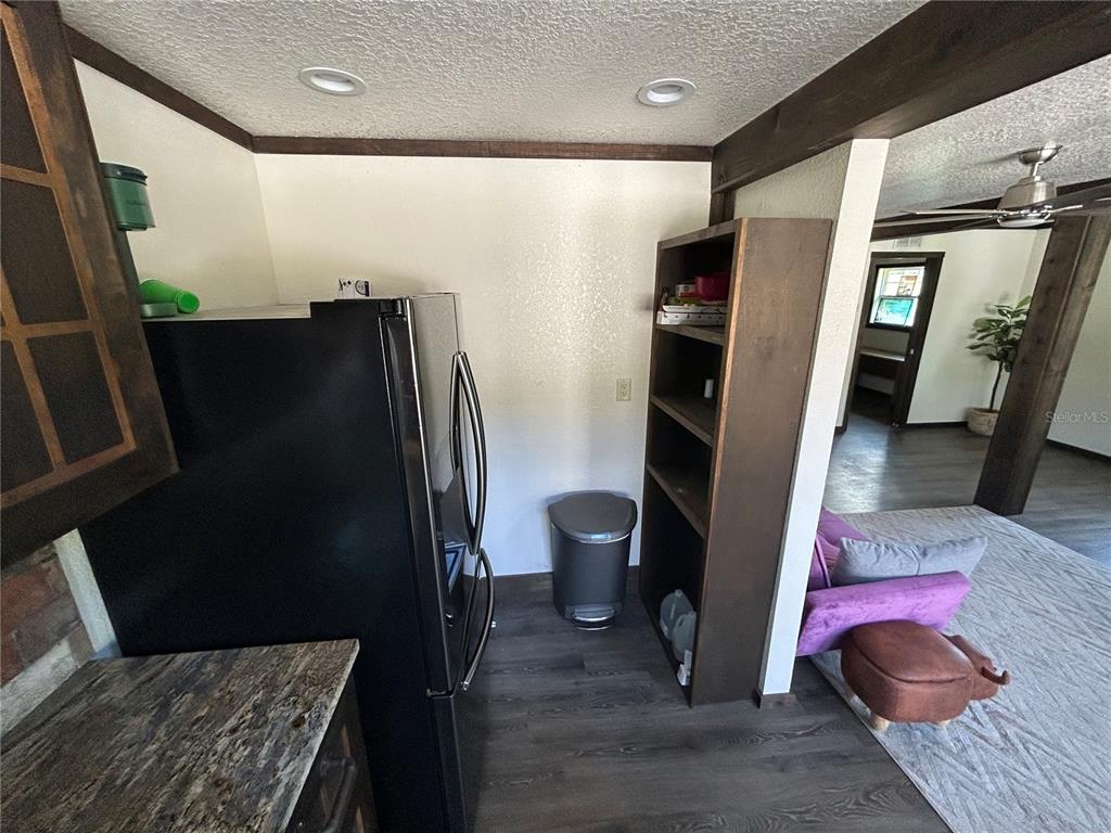 A kitchen area features a black refrigerator, open shelving, and a trash can — 15455 NW 100TH AVENUE ROAD, REDDICK, FL