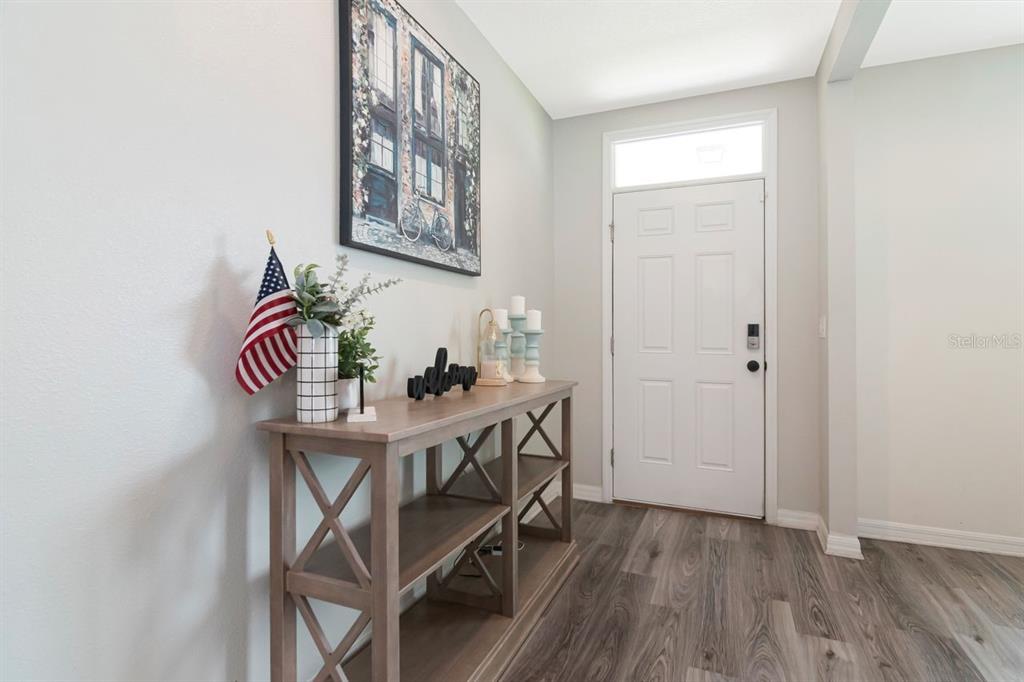 An entryway features a wood console table, wall art, and a white front door — 6803 EZRA LOFT PLACE, ZEPHYRHILLS, FL