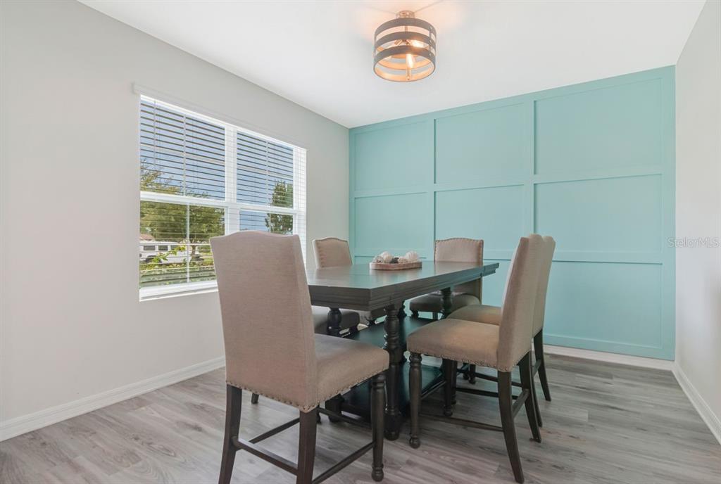 A dining room features a light blue paneled accent wall, dark wood table, and chairs — 6803 EZRA LOFT PLACE, ZEPHYRHILLS, FL