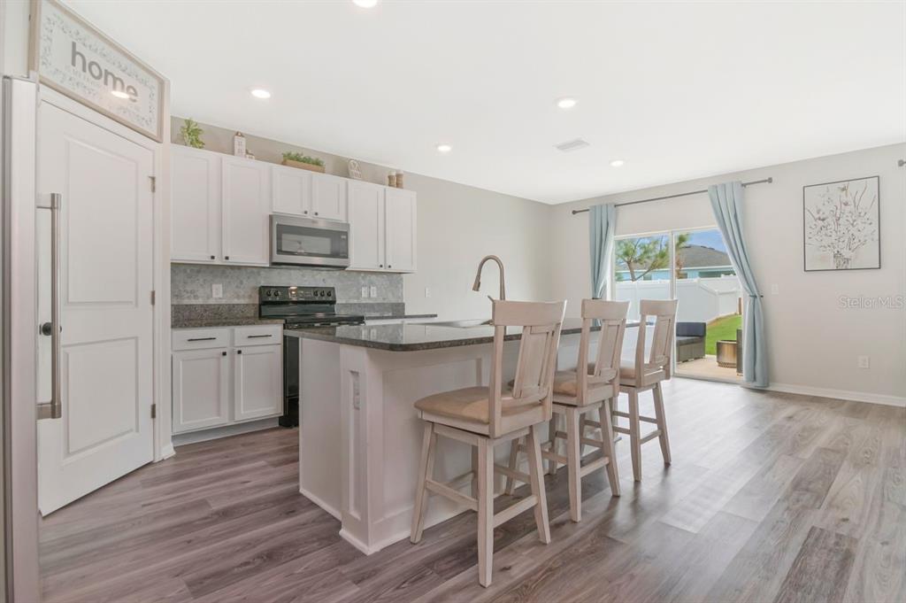 A kitchen with white cabinets, a granite island with three stools, and sliding glass doors — 6803 EZRA LOFT PLACE, ZEPHYRHILLS, FL