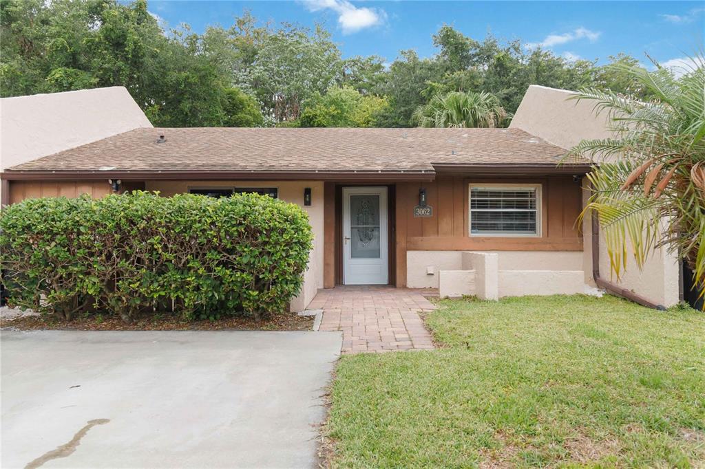 A single-story house with a brown shingled roof, stucco walls, and a large front hedge — 3062 STONECASTLE ROAD, ORLANDO, FL
