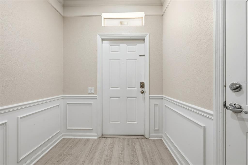An entryway features white wainscoting, light wood-look flooring, and a white door with a transom — 4845 TIDECREST AVENUE UNIT 146, ORLANDO, FL