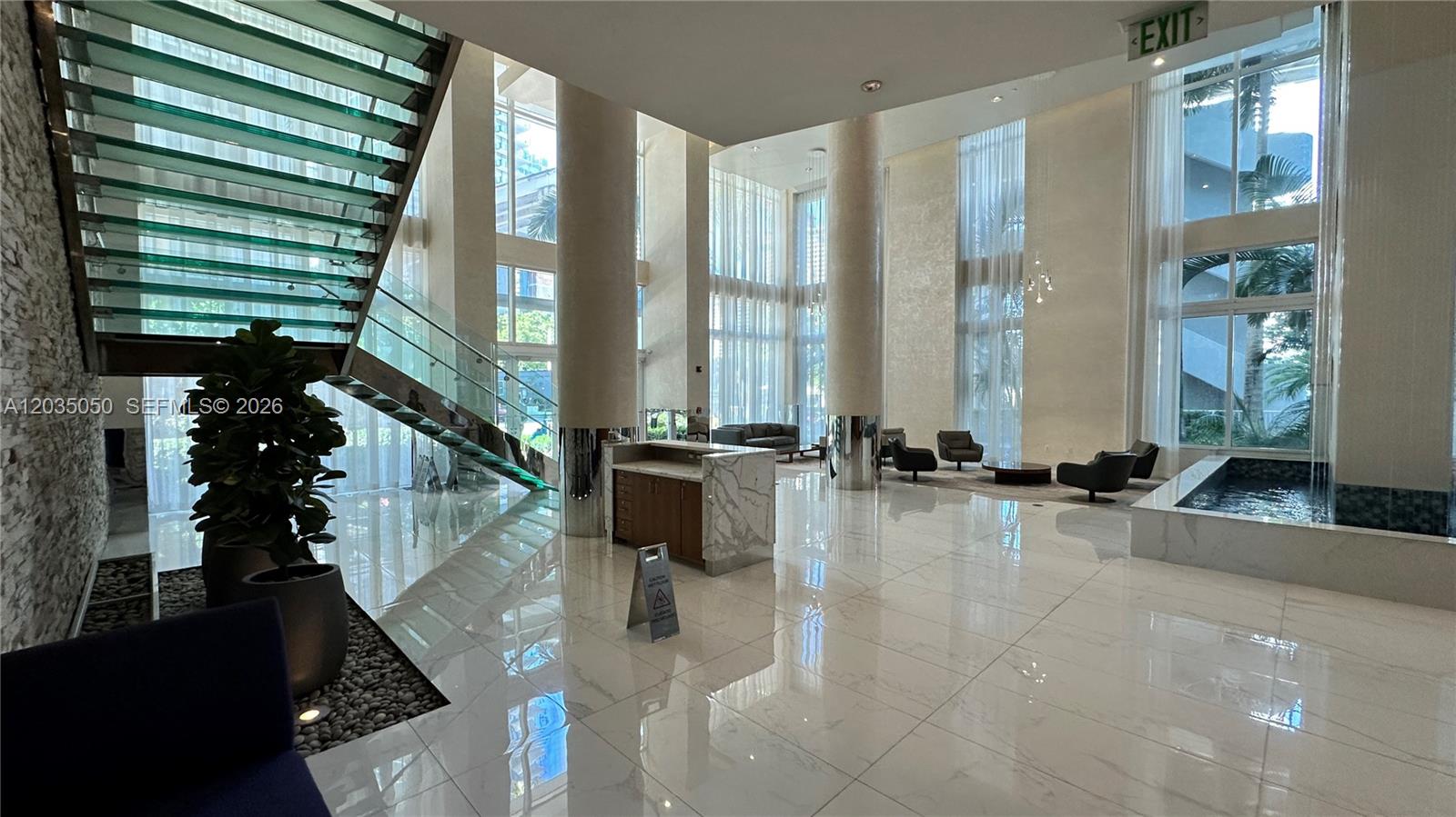 A modern building lobby features a glass staircase, marble floors, and floor-to-ceiling windows — 41 SE 5th St # 1104, Miami FL 33131, MIAMI, FL