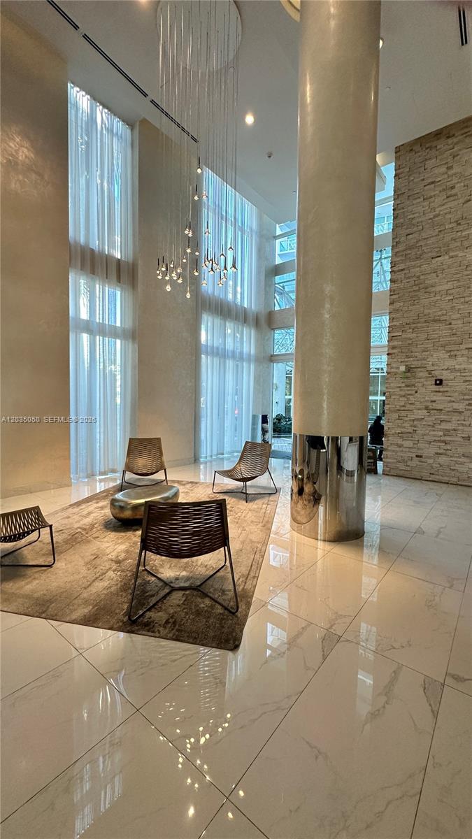 A modern lobby features floor-to-ceiling windows, a large chandelier, marble floors, and contemporary seating — 41 SE 5th St # 1104, Miami FL 33131, MIAMI, FL