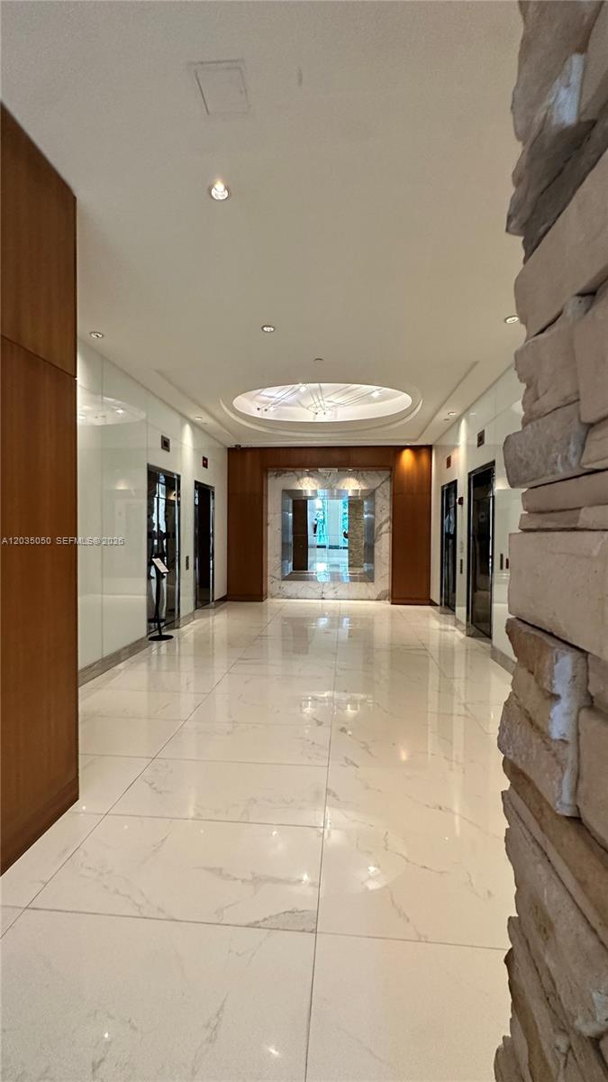 A modern elevator lobby features polished white marble floors, wood paneling, and recessed lighting — 41 SE 5th St # 1104, Miami FL 33131, MIAMI, FL