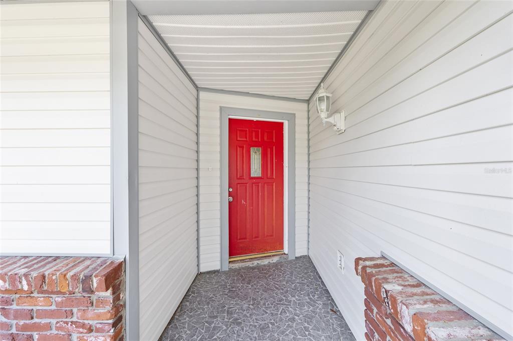 A red front door is centered in a covered porch with white siding and brick accents — 2130 NE 9TH STREET, OCALA, FL