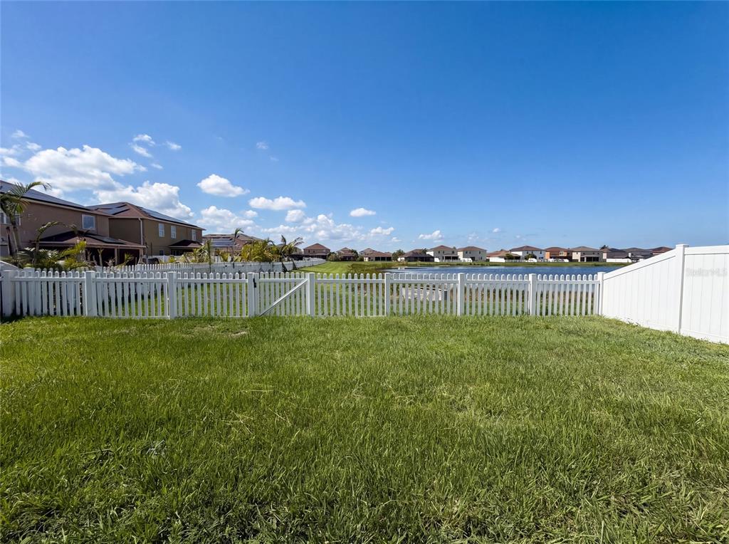 A grassy backyard features a white vinyl fence overlooking a pond and residential houses — 11534 BRIGHTON KNOLL LOOP, RIVERVIEW, FL