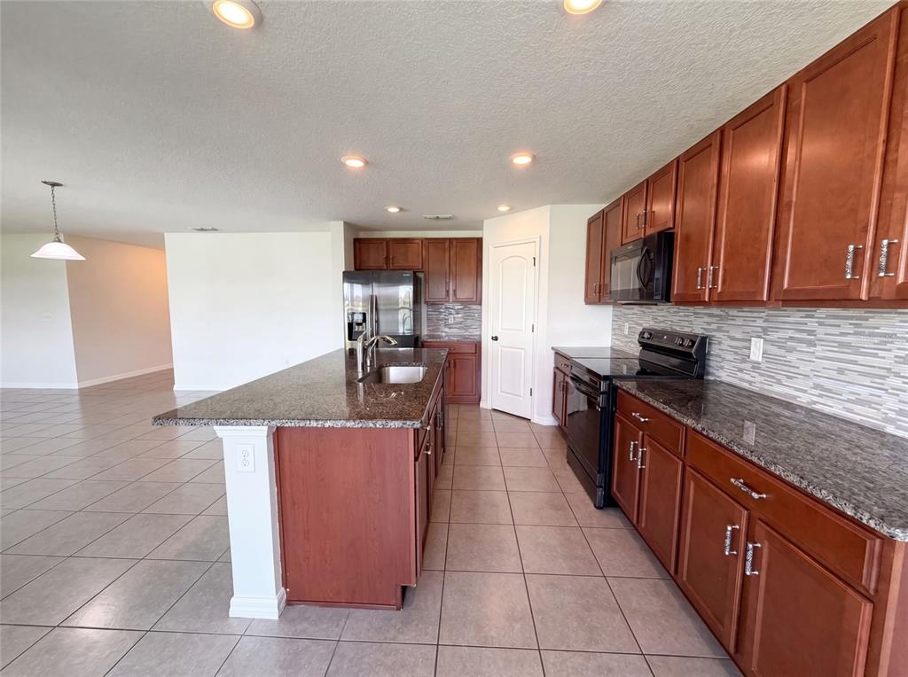 A kitchen features dark wood cabinets, granite countertops, a center island, and tile flooring — 11534 BRIGHTON KNOLL LOOP, RIVERVIEW, FL
