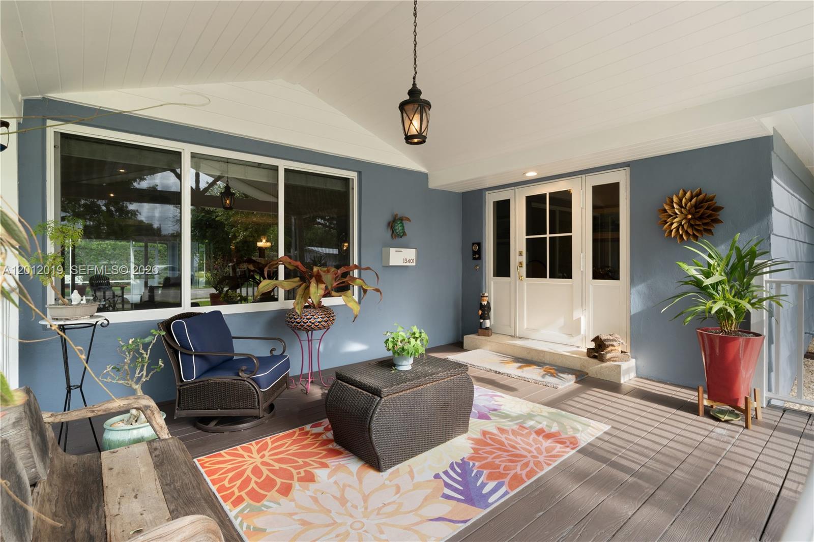 A covered porch features blue walls, a wooden deck, outdoor furniture, and a white front door — 13401 SW 74th Ave, Pinecrest FL 33156, PINECREST, FL